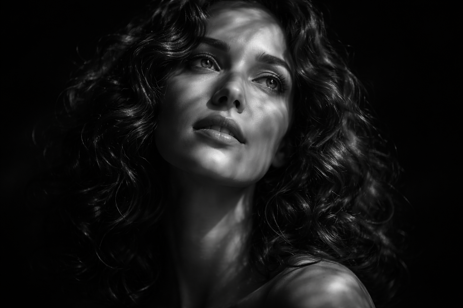 Mujer con cabello rizado, mirando hacia arriba en un contraste de luz y sombra.